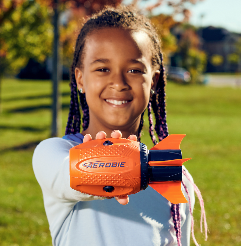 Young girl holding an orange Aerobie Sonic Fin football outdoors ready to throw with a smile