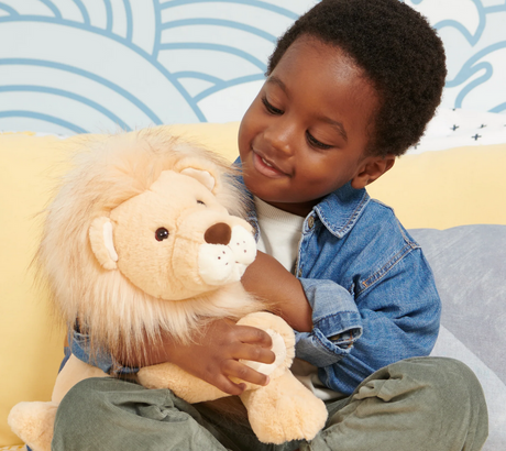 Child hugging the plush Lion Regis with a fluffy two-tone mane and soft tan fur in a cozy playroom.