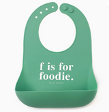 Green silicone bib with adjustable snaps and pocket featuring the phrase "f is for foodie" in white text