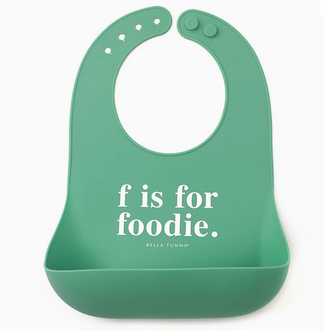 Green silicone bib with adjustable snaps and pocket featuring the phrase "f is for foodie" in white text