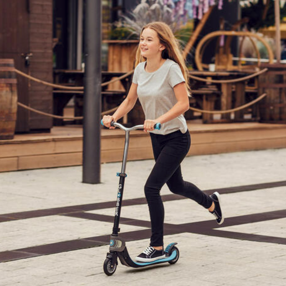 Girl riding a blue Scooter Flow Fold on a paved path with adjustable handlebars and foldable design.