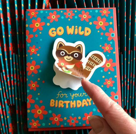 Go Wild Raccoon Sticker Birthday Card with colorful flowers and a playful raccoon sticker being peeled off.