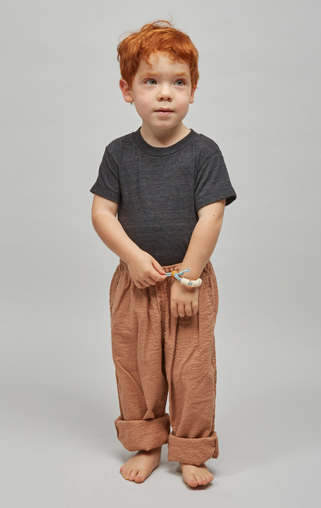Young child wearing the adjustable Adventure Sensory Bracelet | Dune in neutral colors standing barefoot.