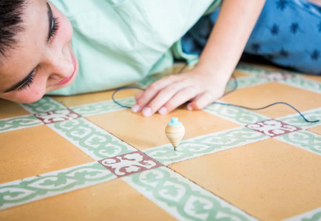 Spinning Top - Mint made of boxwood with blue waxed cotton cord, handcrafted, shown spinning on decorative tile floor.