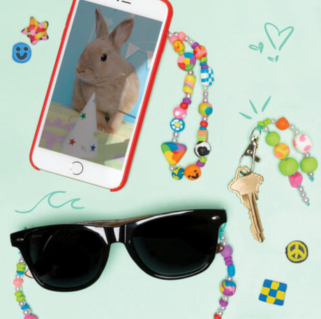 Colorful handmade polymer clay beads and accessories displayed with sunglasses and phone for Ultimate Clay Bead Book.