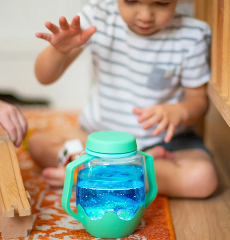 Sensory Jar | Green with spill-proof lid filled with blue water, held by child playing on floor.
