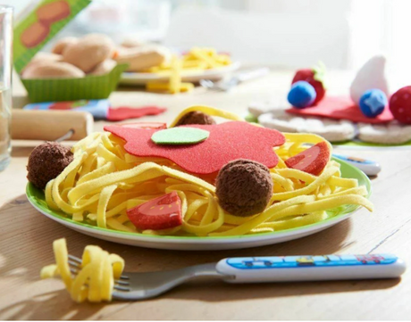 Spaghetti Bolognese play food set with noodles, meatballs, tomato wedges, and basil leaves on a green plate.