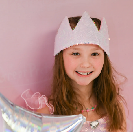 Smiling girl wearing the Ombre Sequins Crown with iridescent sequins and a pink satin bow on a pastel pink background.