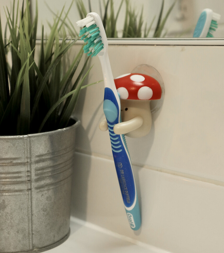 Toothbrush Holder | Mushroom with strong suction holding a toothbrush on a tiled bathroom wall near a potted plant.