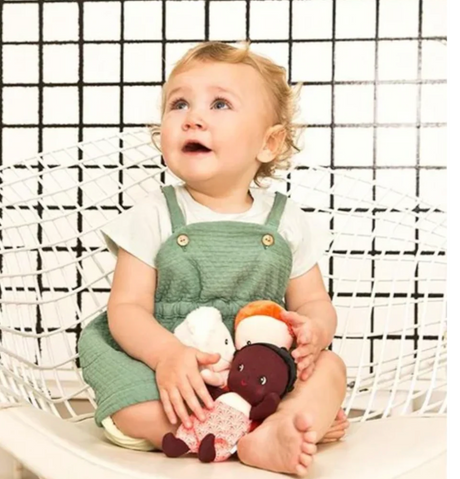 Baby sitting on chair holding My First Baby | Maia doll, designed for easy grasp and early empathy development.
