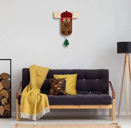 Wood Pendulum Clock | Moose with cozy flannel hat and swinging pine tree pendulum on white wall above sofa.