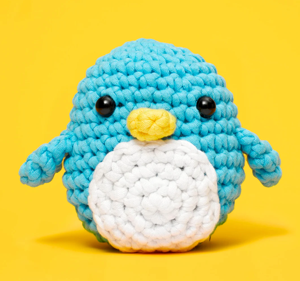 Woobles Crochet Kit Pierre the Penguin featuring a handmade blue and white crocheted penguin with black eyes and yellow beak.