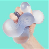 Hand squeezing translucent Speks. Gump Jumbo Dew stress ball with gooey gel inside against blue background.
