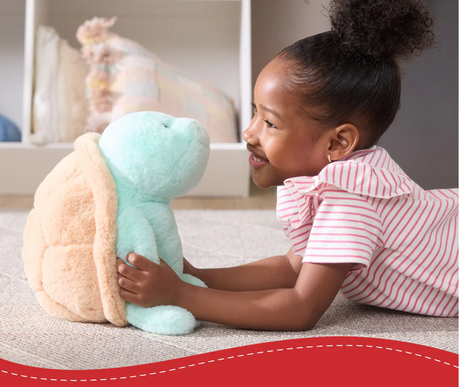 Smiling child playing with Snuffles Sea Turtle plush toy with soft mint-colored fabric and copper shell embroidery.
