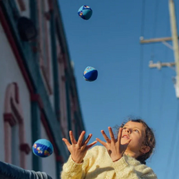 Girl juggling vividly colored balls outdoors with a clear sky backdrop using the Juggling Balls set.