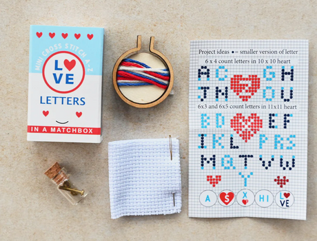 Love Cross Stitch Matchbox showing mini hoop with threads, aida cloth, needle, instructions, and matchbox packaging.