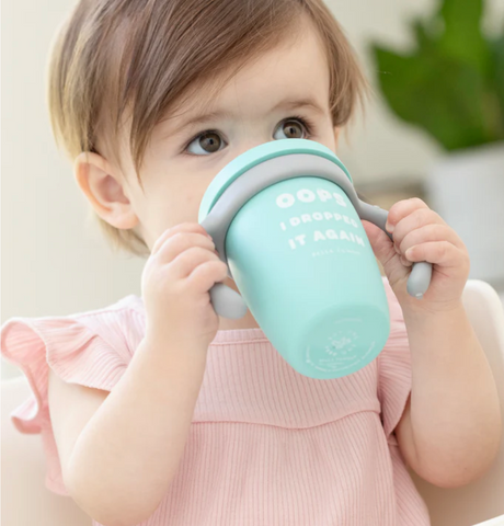 Toddler drinking from a mint green Happy Sippy Cup | Oops I Dropped it Again with handles, spill-proof silicone design.
