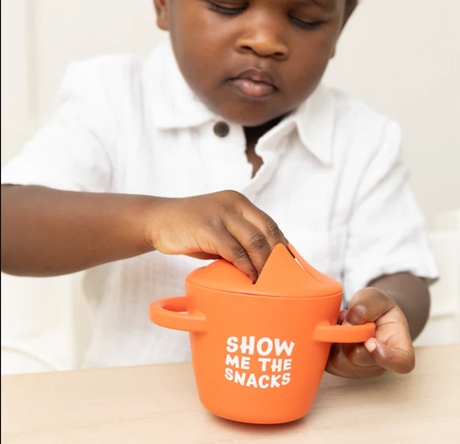 Child using orange Happy Snacker | Show Me the Snacks silicone snack cup with easy grip handles and snap tight lid.