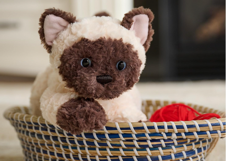 Bootsie Siamese Kitten plush with bright blue eyes, cream and chestnut fur, sitting in a woven basket with a red ball.