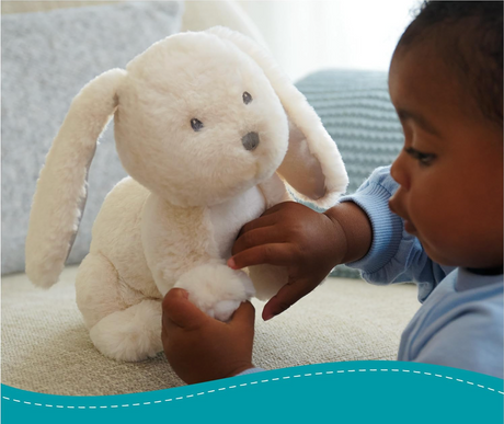 Child holding a soft cream plush bunny with floppy ears, white puffball tail, and embroidered face, Bunny Clover.