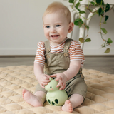 Baby smiling and holding the Silicone Rattle | Dino made of soft, safe silicone for sensory play and motor skill development.