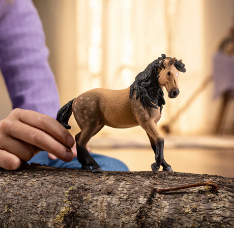 Andalusian Mare toy with fawn coat, black mane, and star-shaped white blaze held by a child on a log.