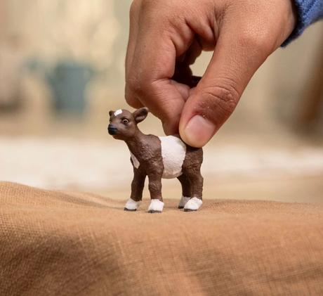 Hand holding a small Goat Kid toy with chocolate brown and white fur and a white spot on its forehead.