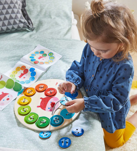 Young child playing with Rainbow Caterpillar Counting Threading Game, threading colorful numbered tiles onto the board.