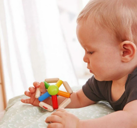 Baby playing with colorful wooden toy held in hands, Color Carousel Wooden Rattle for sensory development.