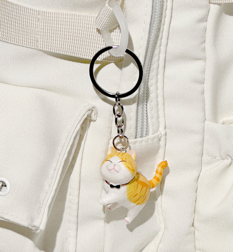 Small orange and white cat keyring with a happy expression hanging from a white fabric bag zipper pull