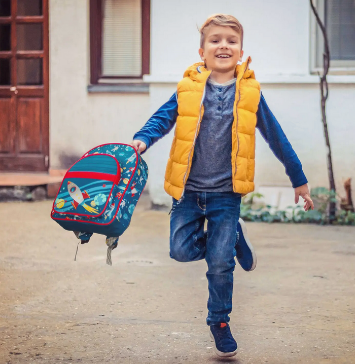 Happy boy jumping outside holding a colorful backpack with a rocket ship pattern on the front pocket
