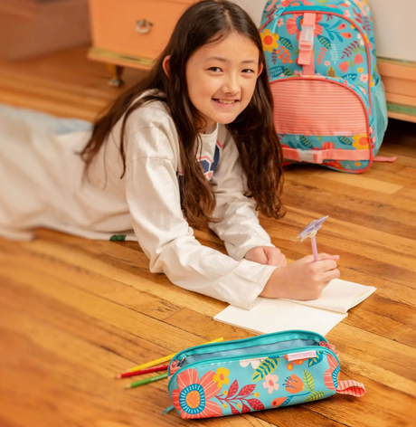 Girl lying on wooden floor writing in notebook with colorful pencil pouch and backpack nearby