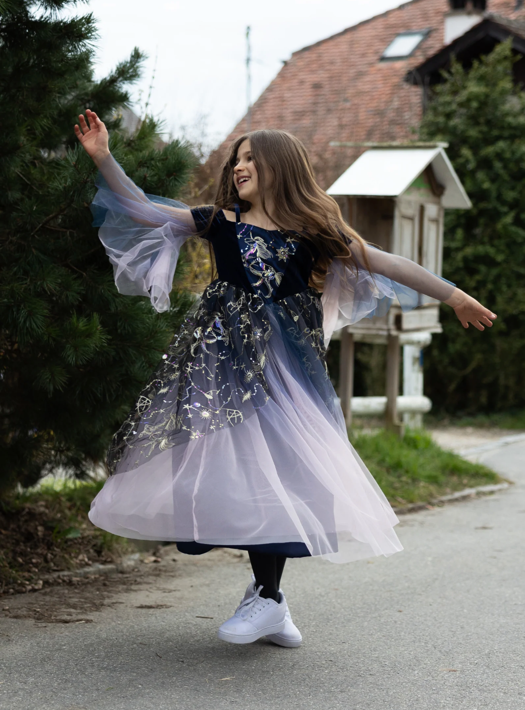 Young girl twirling outdoors wearing a dark purple gown with gold star embroidery and flowing ombré tulle skirt.
