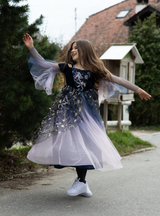 Young girl twirling outdoors wearing a dark purple gown with gold star embroidery and flowing ombré tulle skirt.