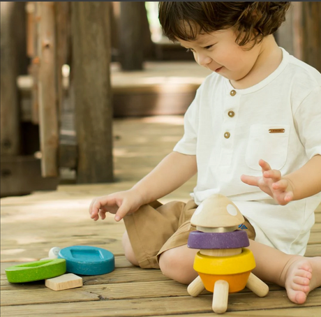 Young child happily stacking colorful wooden rocket pieces on a wooden floor in natural light