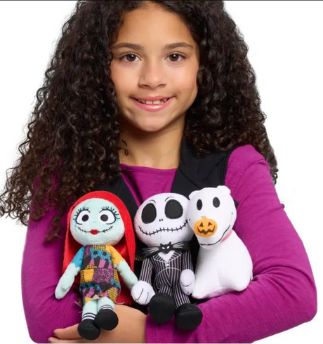 Child holding three plush toys from The Nightmare Before Christmas including Sally, Jack Skellington, and Zero dog.