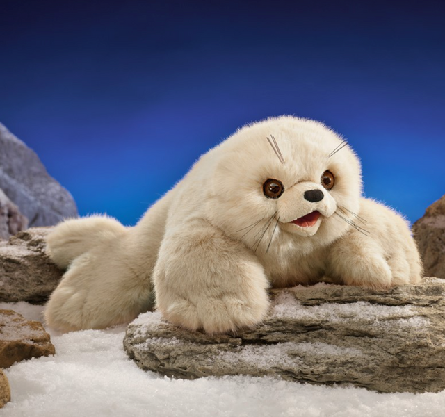 Soft plush harp seal pup puppet with big dark eyes and movable mouth resting on rocks and snow background