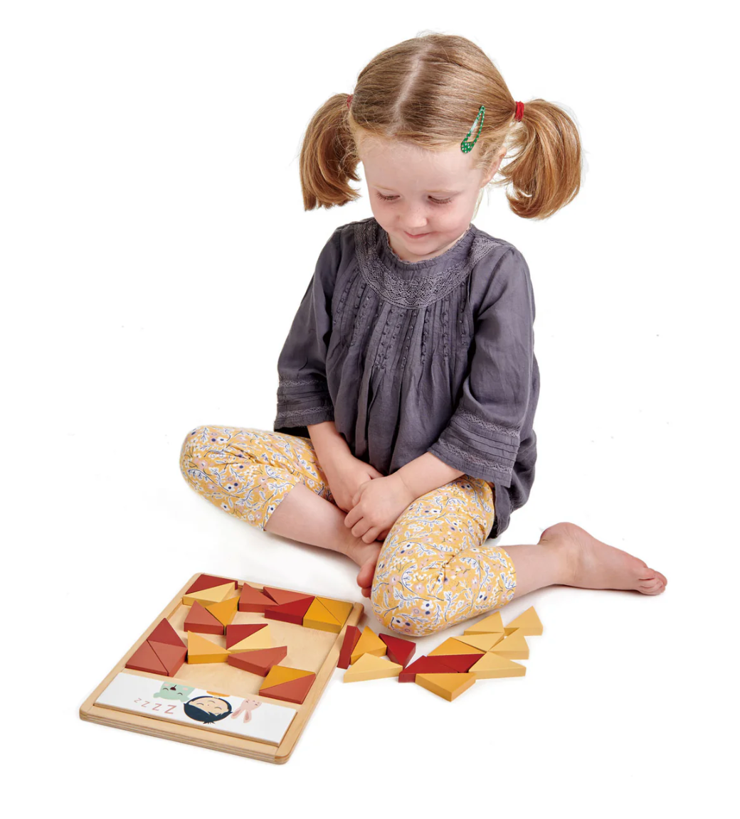 Young girl sitting cross-legged playing with a colorful patchwork quilt puzzle made of triangular pieces