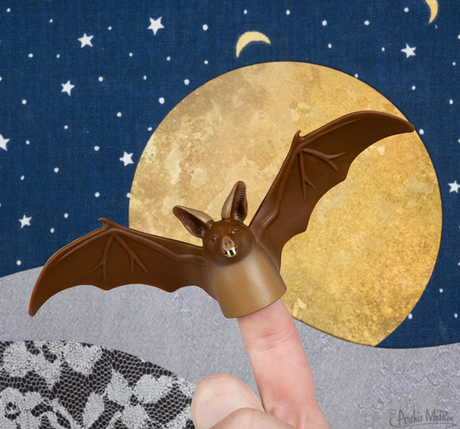Brown bat finger puppet worn on finger with moon and starry night background