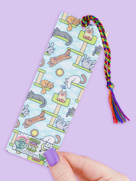 Hand holding a colorful cat tower themed bookmark with a rainbow tassel on a pastel background