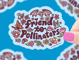 Hand holding colorful "friend to pollinators" sticker surrounded by bees, butterflies, flowers, and a bat on blue background