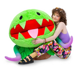 Young woman sitting and hugging a large plush green Venus Fly Trap plant with colorful details and wide open mouth