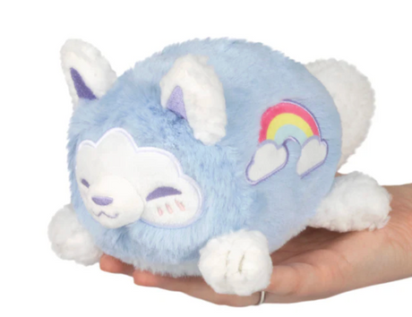 Small blue and white plush kitsune with a rainbow patch, resting on a hand, soft and cuddly toy for all ages.