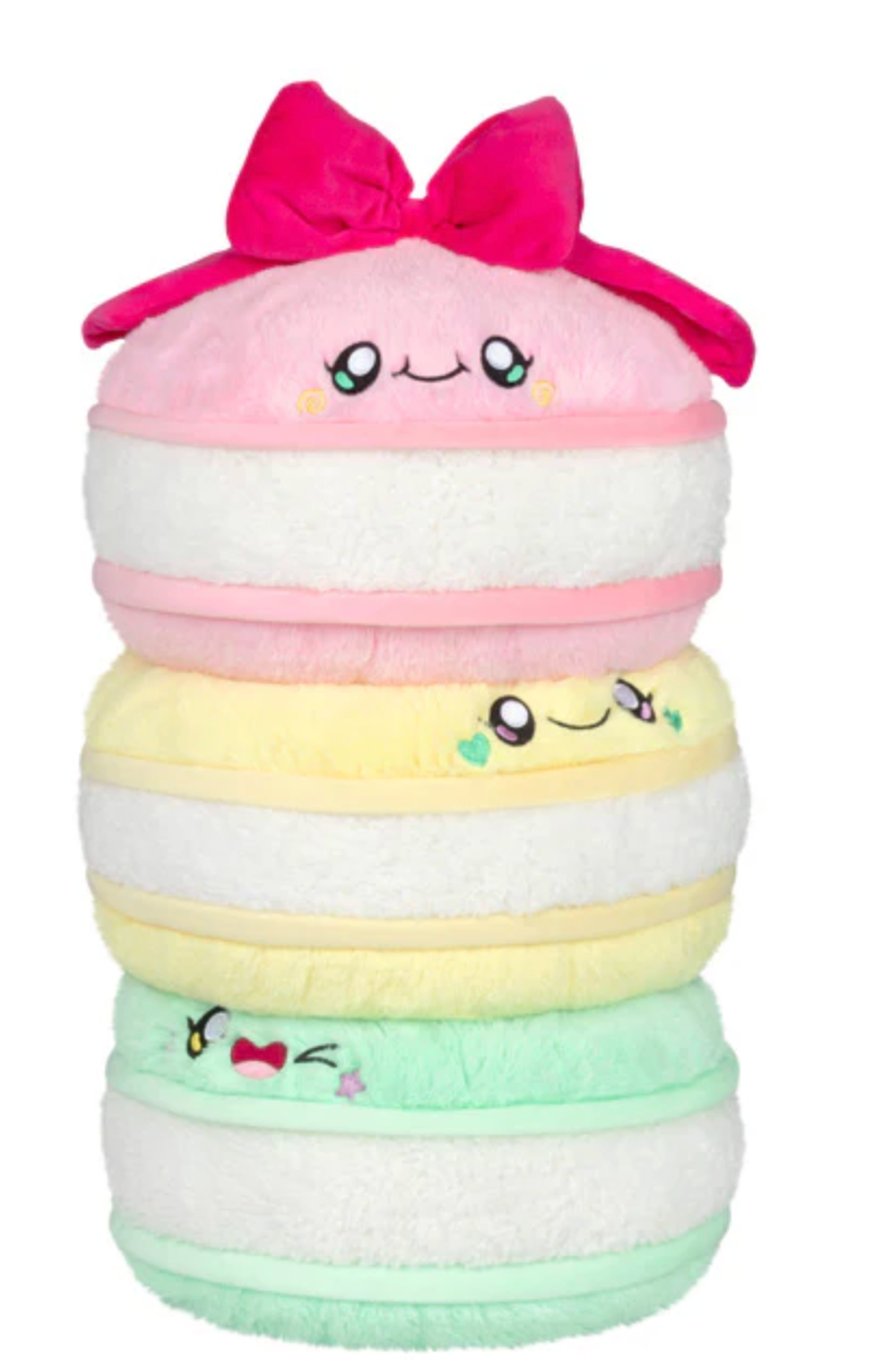Stack of three soft plush macarons in pastel pink, yellow, and green with cute smiling faces and a bow on top