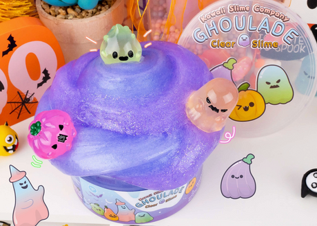 Purple glittery slime with three cute Halloween ghost charms and spooky decorations in the background