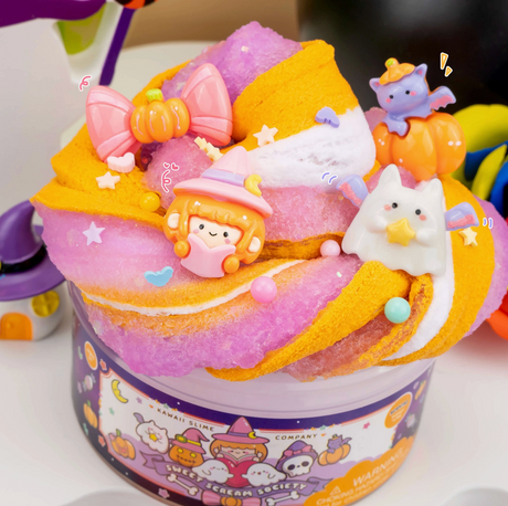 Swirled orange, white, and purple slime topped with cute Halloween charms including a ghost, pumpkin kitty, witch, and sprinkles