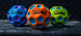 Three colorful high-bounce Waboba Moon Balls with crater grip design on a textured dark surface