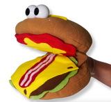 Hand puppet shaped like a hamburger with cheese, lettuce, bacon, and large cartoon eyes being worn on a hand