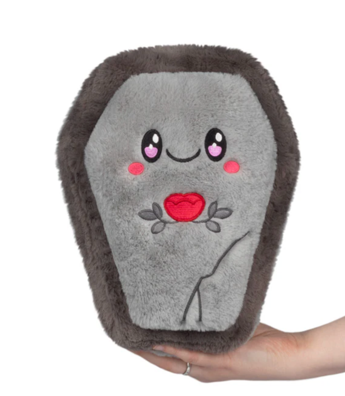 Soft gray coffin-shaped plush toy with a smiling face and red heart embroidery held in hand