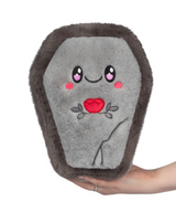 Soft gray coffin-shaped plush toy with a smiling face and red heart embroidery held in hand